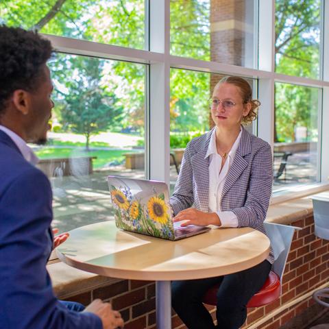 Two students talking in the MUC buy the windows. 